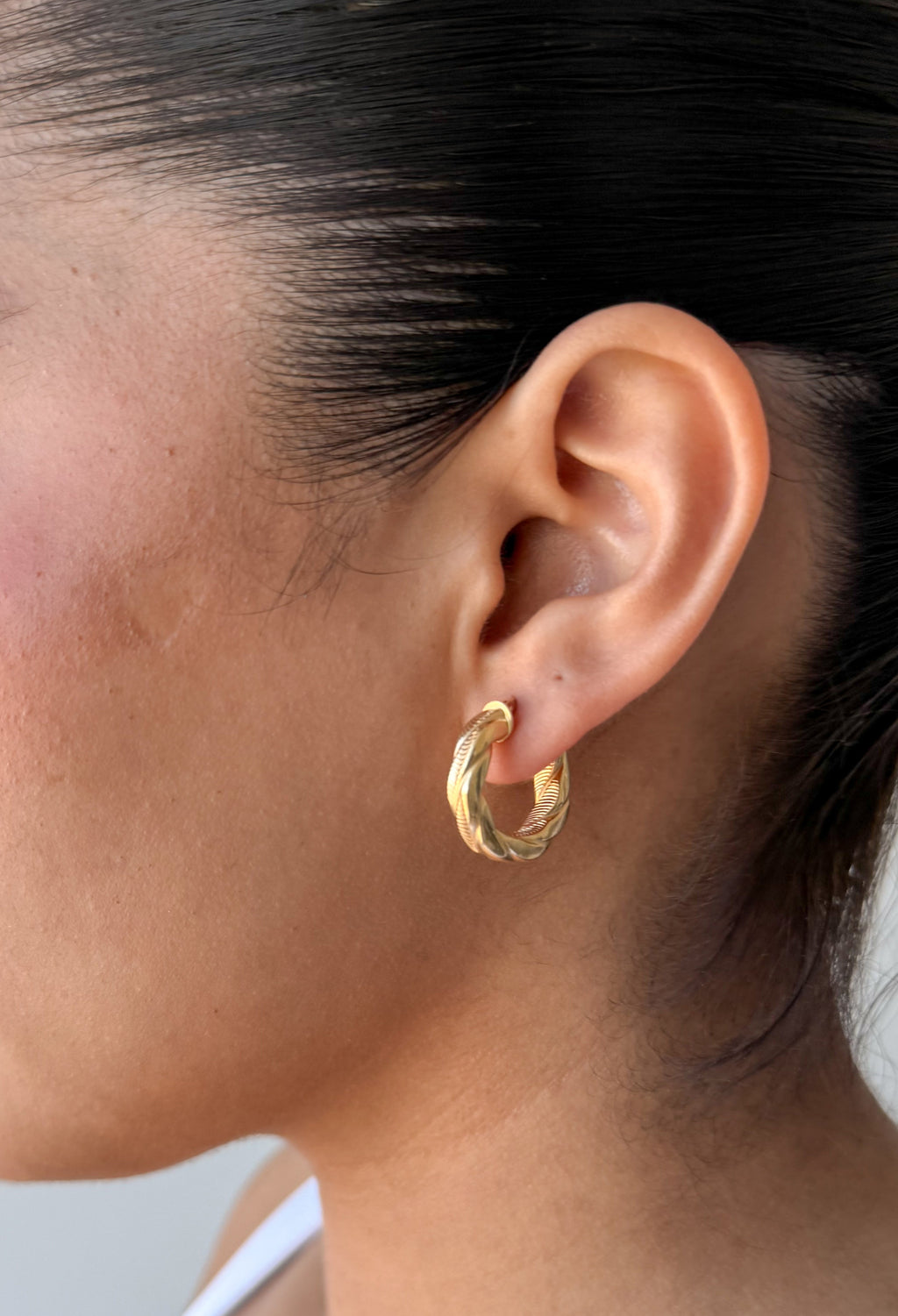close-up of model wearing senoe twisted hoop earrings in 14k yellow gold 